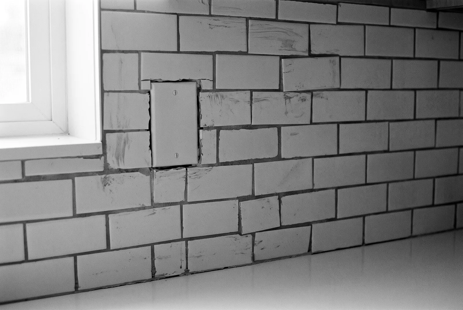 Render of a newly tiled kitchen backsplash with wandering grout lines, grout haze and tiles cut unevenly around a blank outlet cover.