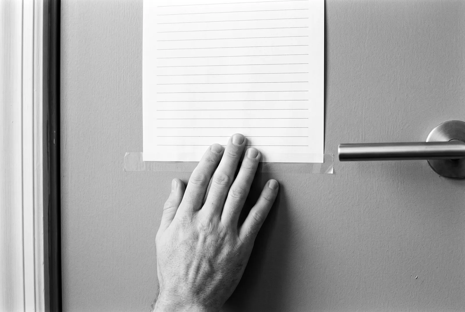 Render of a hand pressing tape onto a blank lined sheet of paper fixed to a painted door beside a lever handle.