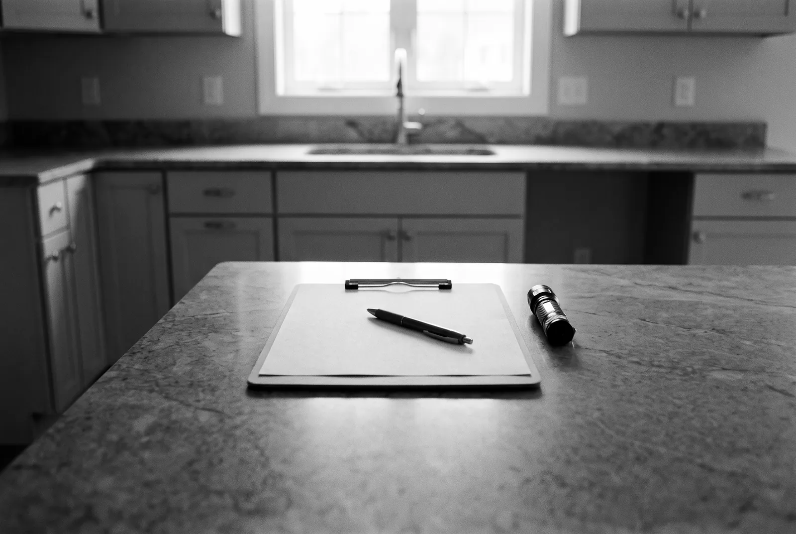 Render of a clipboard with a blank sheet, a pen and a small flashlight on a new stone kitchen counter.