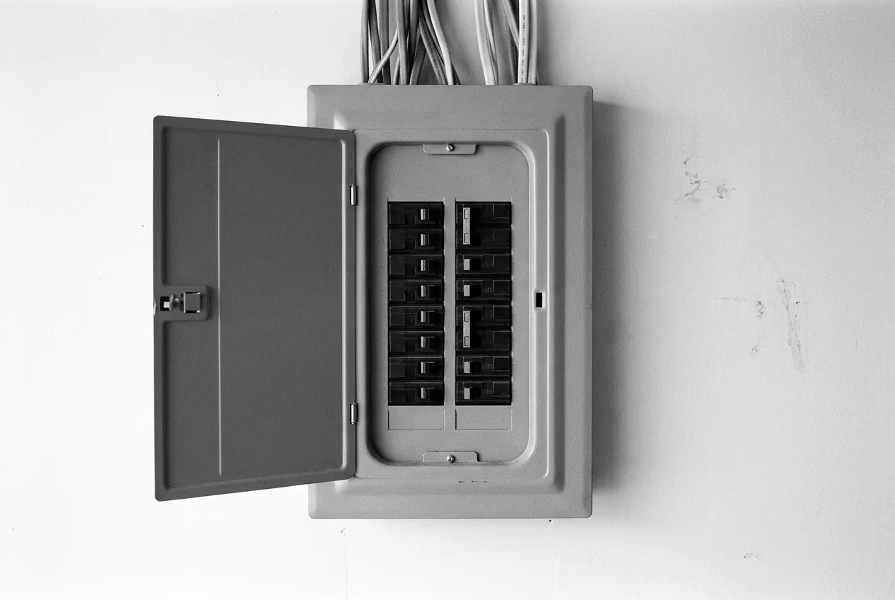 Render of a home electrical panel on a garage wall, its door open on two columns of breakers.