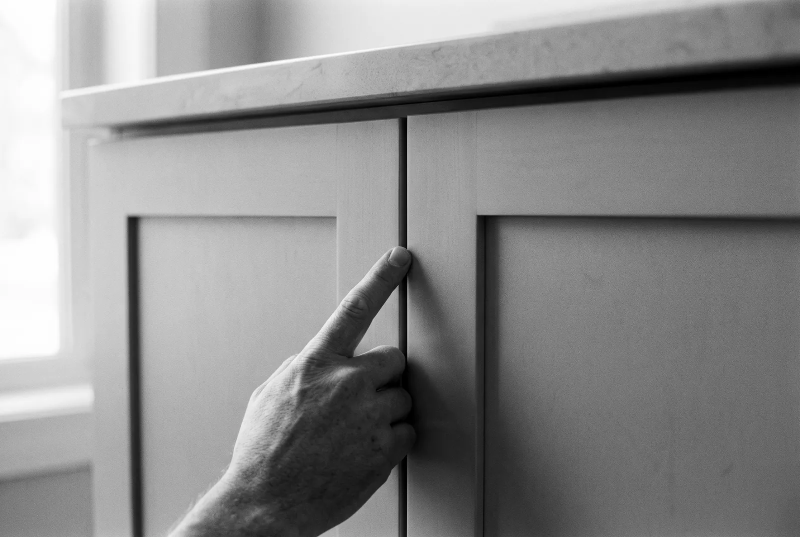 Render of a finger running along the gap between two shaker cabinet doors under a stone countertop edge.