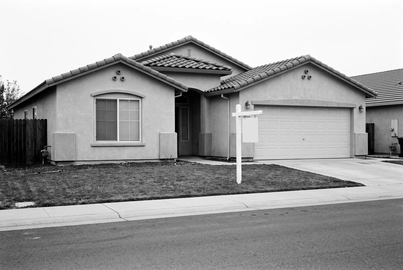Render of a single story stucco house with a tile roof and a two car garage, a blank sign post on the lawn.