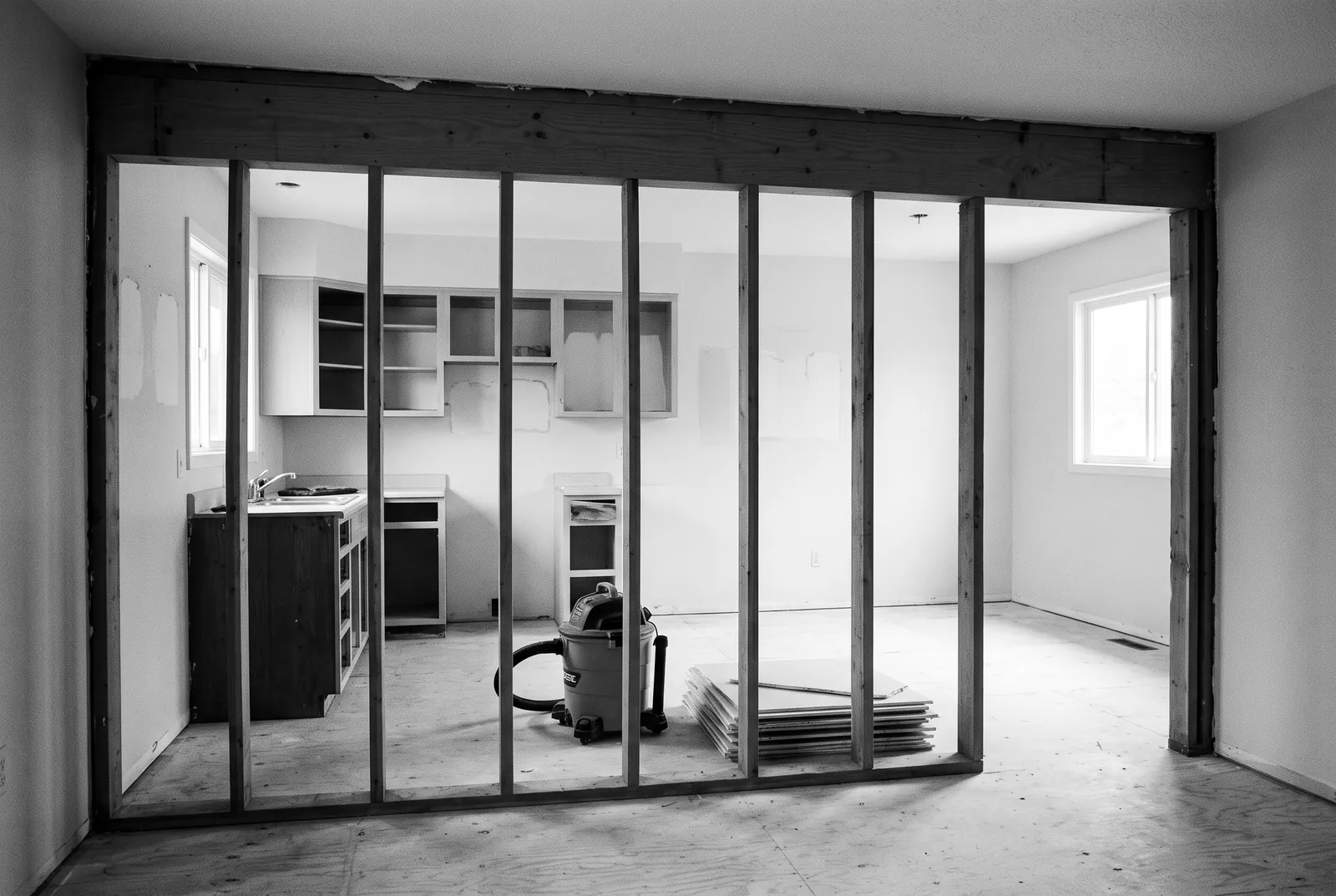 Render of a wall between a kitchen and a dining room opened to bare studs under a new header beam, with the old cabinets half removed beyond it.