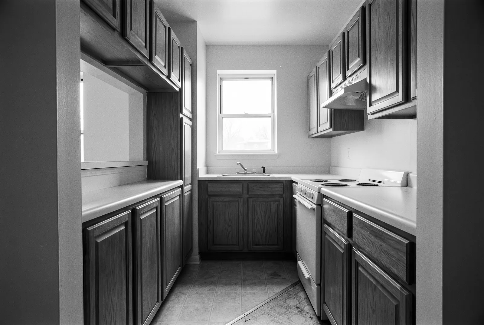 Render of a narrow older kitchen with oak cabinets on both sides, a white range, a pass through opening and a window over the sink.