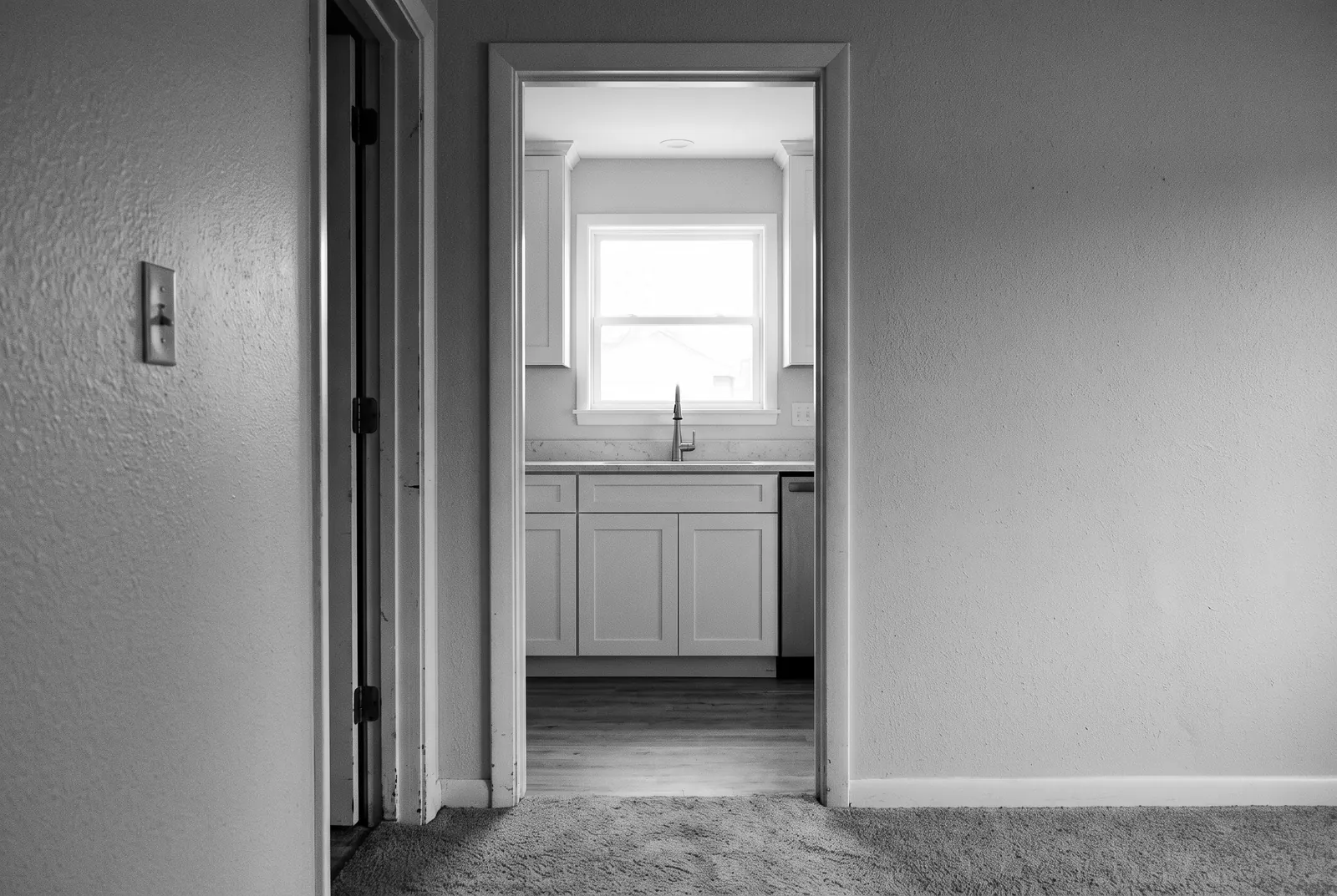 Render of a freshly remodeled kitchen seen through a doorway from an older carpeted hallway with textured walls.