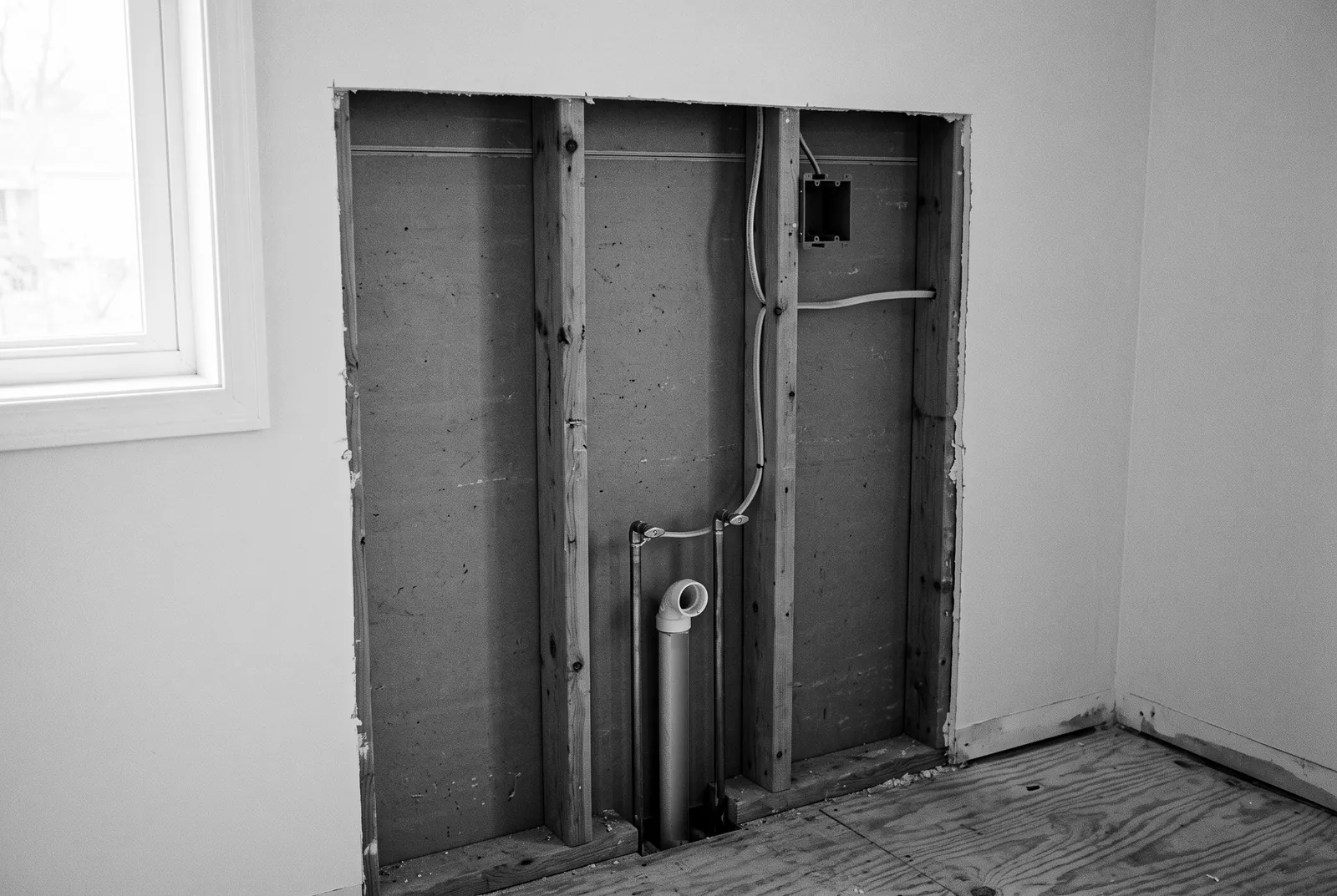 Render of a wall opened to the studs, with water pipes and a drain rising from the floor and a new electrical box on a stud.