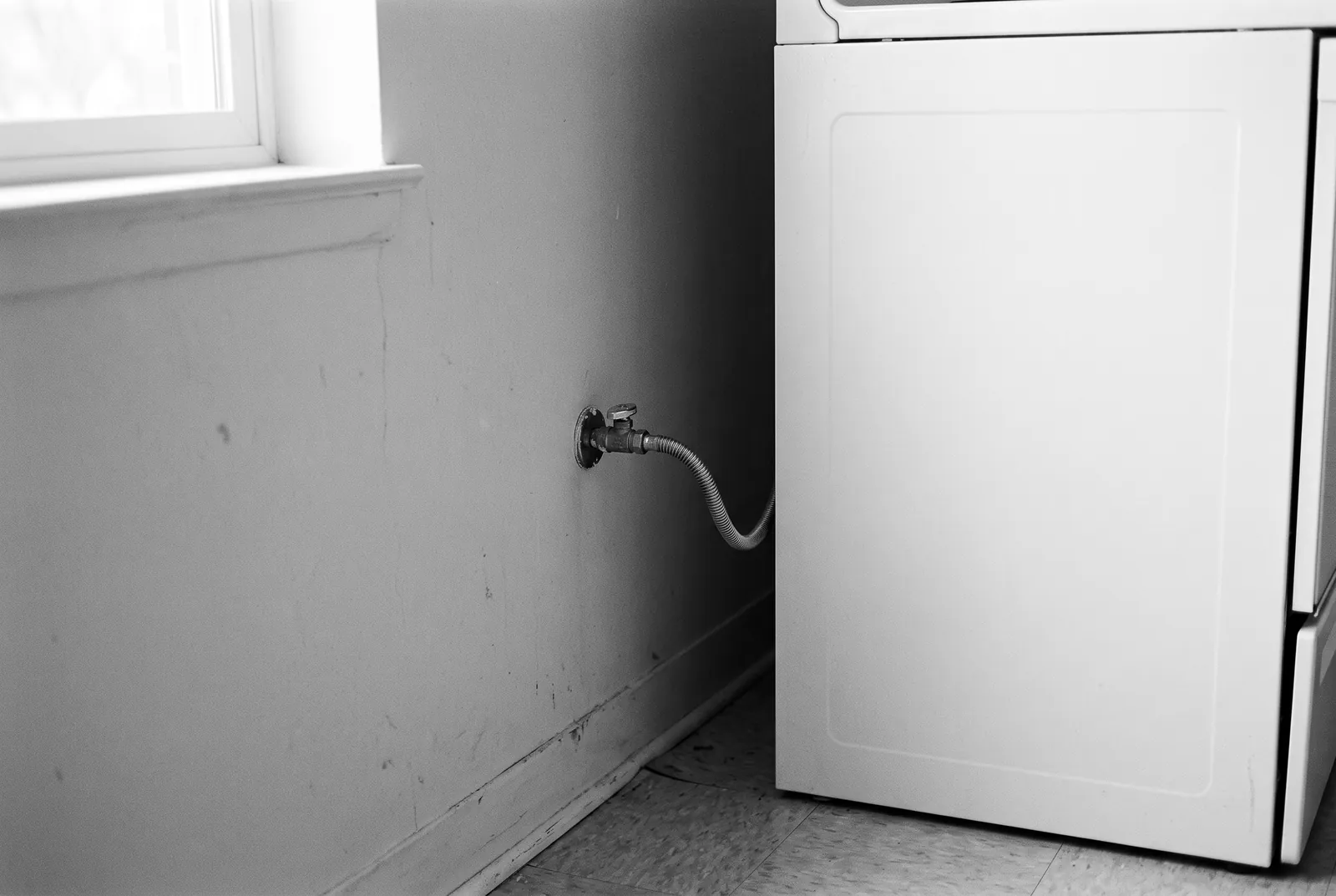 Render of a shutoff valve on a wall with a flexible metal connector running to the side of a white appliance.