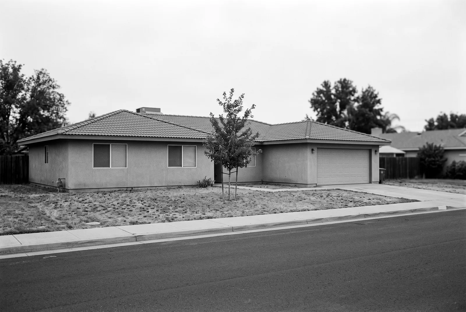 Render of a single story stucco house with a tile roof and a two car garage, seen from across a quiet street.
