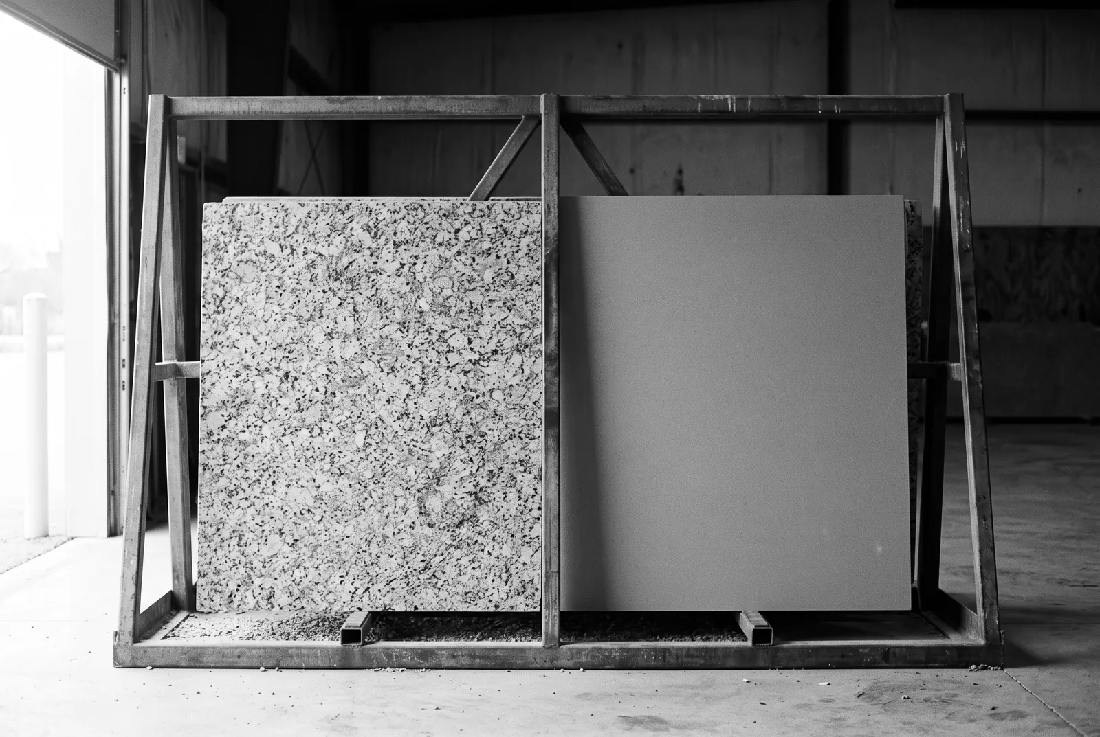 Render of two countertop slabs side by side in a steel rack, one with a busy speckled crystal pattern and one smooth and even in tone.