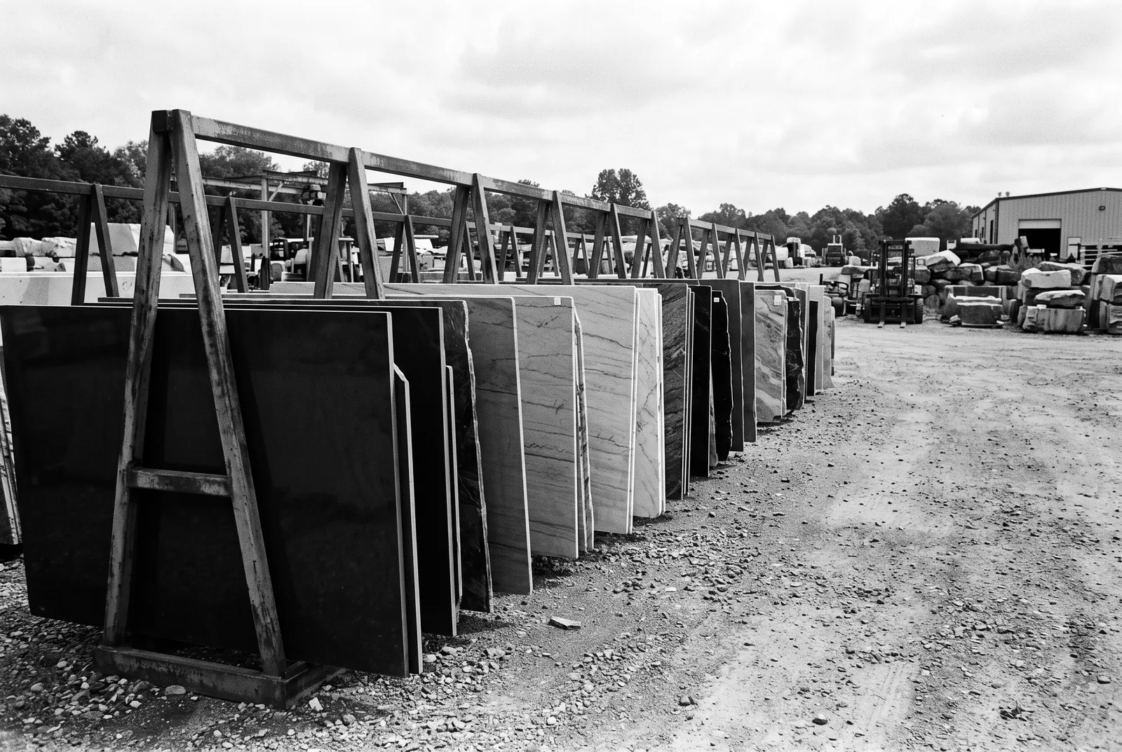 Render of a long row of polished countertop slabs standing on edge in steel racks in an outdoor stone yard.